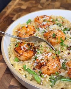 a white bowl filled with pasta and shrimp on top of a wooden table next to a fork