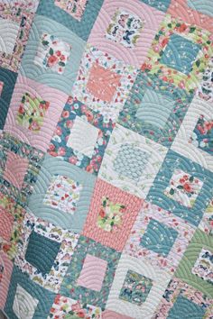 a close up of a quilt on a bed with pink, blue and green colors