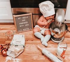 a baby doll sitting on the floor next to a mixer and other kitchen items, including utensils