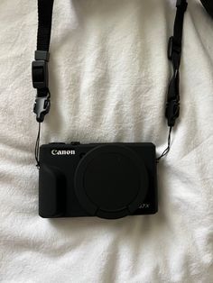 a black camera sitting on top of a white bed next to a strap that is attached to it