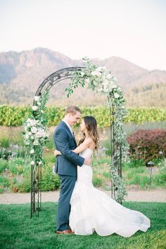 a bride and groom standing under an arch with greenery at their wedding in the mountains