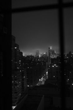 the city skyline is lit up at night in black and white, as seen from an apartment window