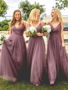 three bridesmaids in purple dresses laughing and standing on the grass with their bouquets