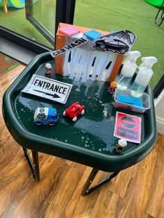 a green table topped with lots of toys and bottles on top of wooden flooring