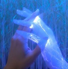 a hand is holding plastic bags in front of tall grass with blue lights shining on them