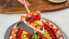 someone cutting into a fruit pizza with a knife