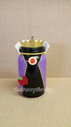 a purple and black jar with a gold crown on it's head sitting on a table