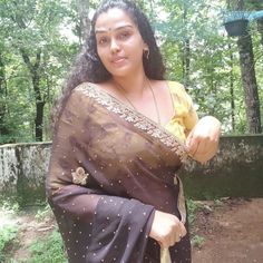 a woman in a sari holding an umbrella and posing for the camera with trees in the background