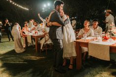 a couple hugging each other in front of a group of people at a dinner table