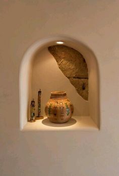 a vase sitting on top of a white shelf next to a stone wall under a light