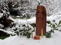 a wooden statue and two candles in the snow