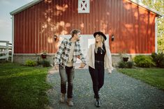 a man and woman walking in front of a red barn with a black hat on