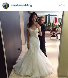 a woman in a wedding dress taking a selfie with her cell phone while standing next to a man