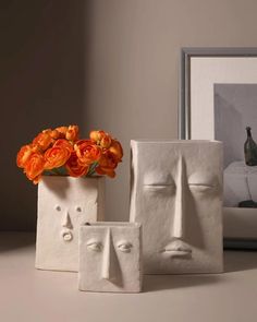 two white vases with orange flowers in them sitting on a table next to a framed photograph