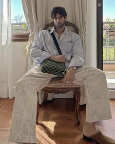 a man sitting on top of a wooden chair in front of a window with curtains