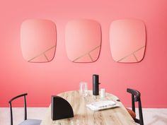 a dining table with four chairs and three mirrors on the wall above it, in front of pink walls