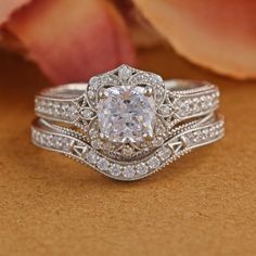 a white diamond ring sitting on top of a wooden table next to a flower bouquet