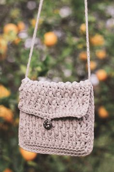 a crocheted purse hanging from a tree with oranges in the back ground