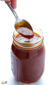 a spoon full of jam being held by a person's hand over a jar