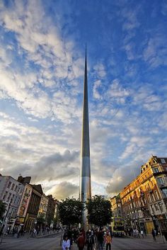 people are walking around in front of a very tall building with a spire on top