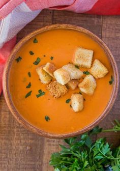 a bowl filled with soup and croutons on top of a wooden table next to parsley