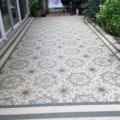 an outdoor patio with white and grey tiles on the floor, surrounded by greenery