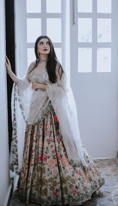 a woman in a long dress standing by a window with her hands on her hips