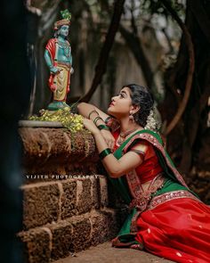 a woman in a red and green sari sitting on the ground next to a statue