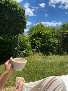 a person laying on the ground holding a cup of coffee in their hand and looking up into the sky