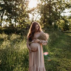 a pregnant woman standing in the grass with her hands on her belly and holding flowers