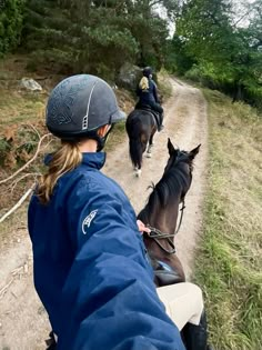 two people riding horses down a dirt road