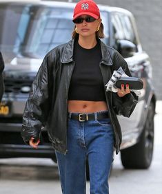 a woman walking down the street wearing jeans and a black top with a red hat