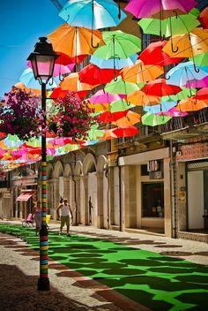 there are many colorful umbrellas hanging in the air on this street side by side