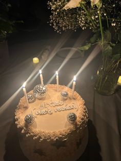 a birthday cake with lit candles and flowers in the background