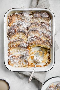 a baked dish with powdered sugar on top and two cups of coffee next to it