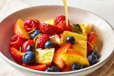 fresh fruit salad with oranges, strawberries and blueberries being poured into a bowl