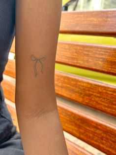 a woman's arm with a small bow tattoo on the left side of her arm