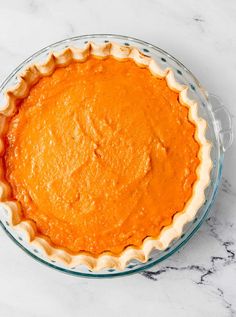 an orange pie sitting on top of a white counter next to a glass bowl filled with it