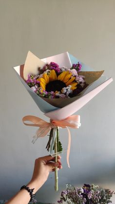 a person holding a bouquet of flowers in front of a white wall with purple and yellow flowers