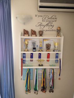 a wall mounted shelf filled with trophies and medals next to a window covered in blue curtains