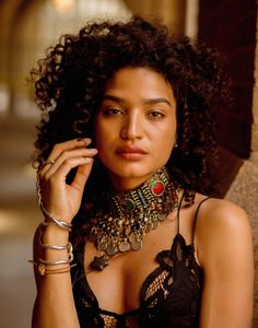 a woman with curly hair wearing a necklace and bracelets on her neck is looking at the camera