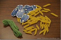 several pieces of pasta and green string on a wooden table with paper cut outs in the shape of fish