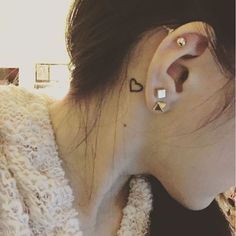 a woman with a heart tattoo on her left side behind the ear, wearing a white sweater