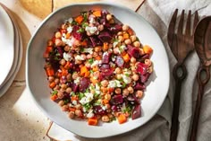 a white bowl filled with lots of food on top of a table next to utensils