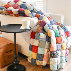 a white couch covered in colorful pillows next to a table with a cup on it