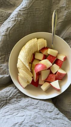 sliced apples and bananas in a white bowl on a bed with a spoon sticking out of it