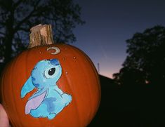 a hand holding up a painted pumpkin with an image of a blue dog on it