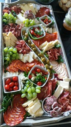 an assortment of meats and cheeses on a platter with olives, tomatoes, grapes, bread