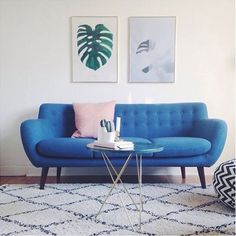 a living room with a blue couch, coffee table and two paintings on the wall