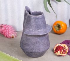 a purple vase sitting on top of a table next to an orange and other fruit